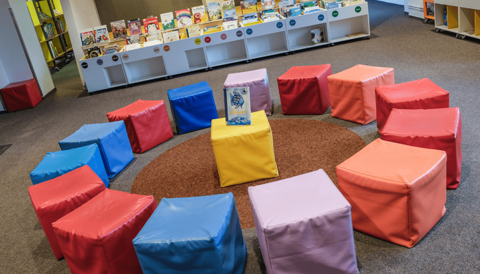 Kinder sitzen im Kreis um eine Frau und blicken interessiert auf das Buch, das sie zeigt