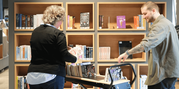 zwei Bibliotheksmitarbeitende stellen Bücher ein